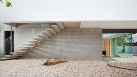 A modern concrete structure with an intricate staircase and glass walls, surrounded by gravel.