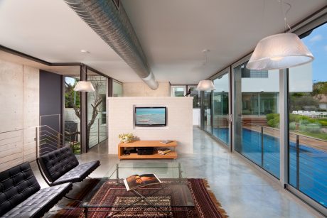 Spacious minimalist living room with glass walls offering pool view and ample natural light.