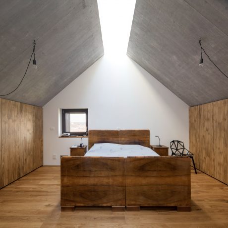 Minimalist bedroom with exposed concrete walls, wooden platform bed, and angular side tables.