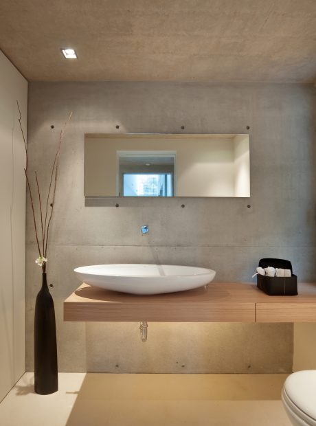 Minimalist bathroom design with a white sink basin, wood vanity, and concrete walls.