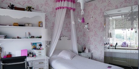 Whimsical, pink-themed bedroom with floral wallpaper, canopy bed, and storage shelves.