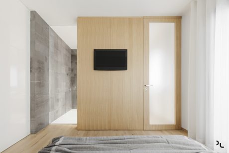 Minimalist bedroom with wooden paneling, full-length mirror, and recessed TV.
