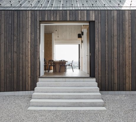 Wooden exterior with concrete steps leading to an interior with modern geometric chairs.