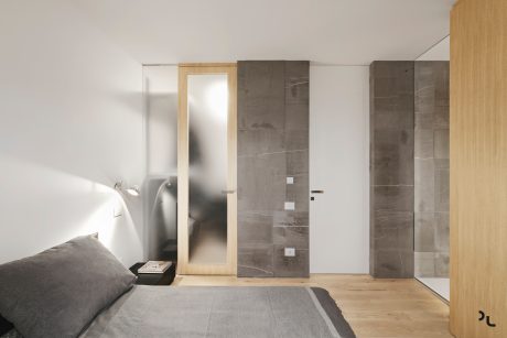 Minimalist bedroom with wooden accents, sleek mirror, and gray marble-like tiles.