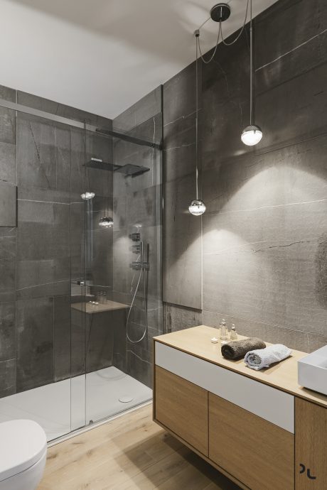 Modern bathroom with a glass shower enclosure, sleek dark tiles, and a wooden vanity.