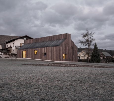 A modern, wooden-clad building with large windows and a sloped roof in a rural landscape.