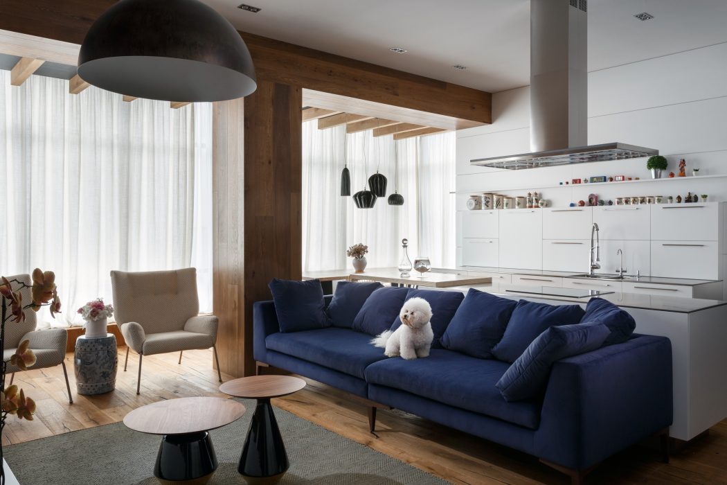 Cozy, rustic living space with exposed wooden beams, navy blue sofa, and modern pendant light.