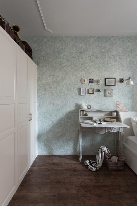 A cozy bedroom with a vintage-style writing desk and shelves, accented by patterned wallpaper.