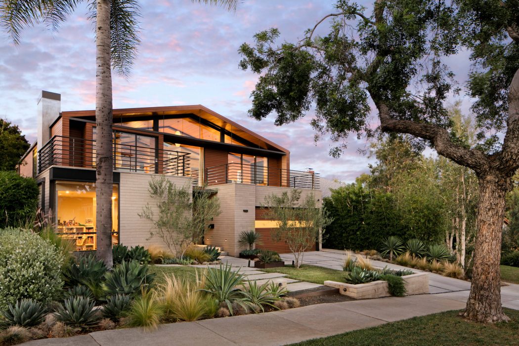 Modern home with wooden siding, floor-to-ceiling windows, and lush landscaping.