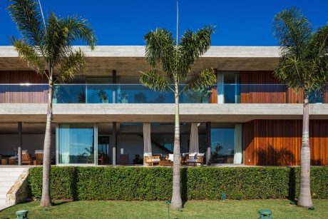 Striking modern beachfront villa with large balconies, palm trees, and lush landscaping.
