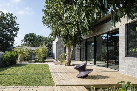A modern exterior with a wooden deck, glass walls, and sculptural seating in the yard.