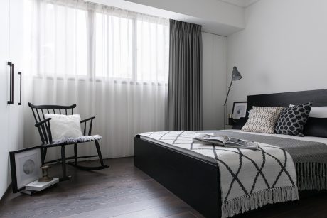 A minimalist bedroom with a black bed frame, patterned bedding, and a rocking chair by the window.