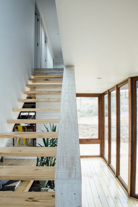 A modern, minimalist staircase with open shelves and large windows overlooking nature.