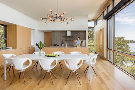 Modern, open-concept kitchen and dining area with large windows, sleek furniture, and a nature-inspired chandelier.