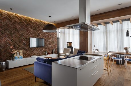 A modern open-plan living space with a brick feature wall, sleek kitchen, and wooden floor.