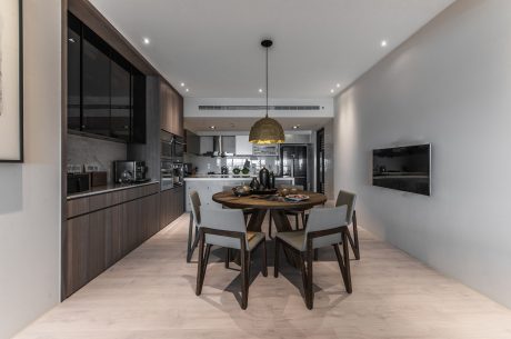 A modern, open-concept kitchen and dining area with sleek wood cabinetry, a round table, and pendant lighting.
