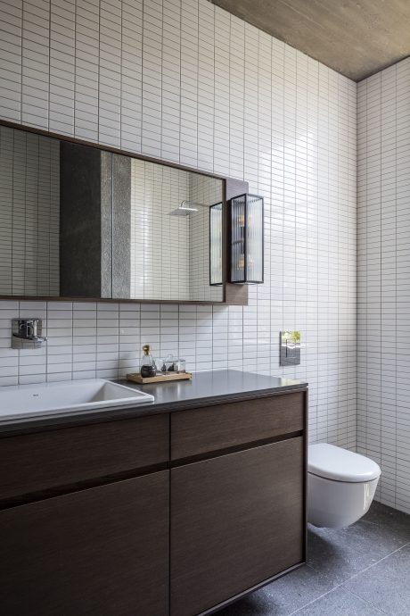 A modern bathroom with a white tile wall, dark vanity, and minimalist light fixtures.