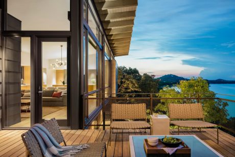 Wooden deck with wicker furniture overlooking lush foliage and a scenic lake view.