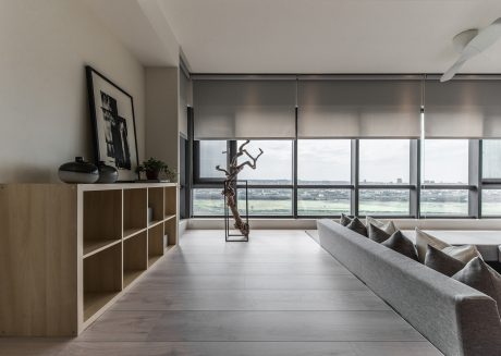 Minimal, modern living room with large windows and wooden cabinetry, showcasing a sculptural artwork.
