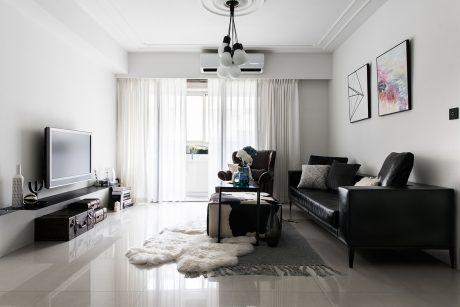 A modern, minimalist living room with sleek black furniture, plush white rug, and a stylish chandelier.