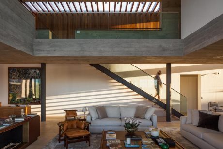 Spacious, modern living room with concrete, wood, and glass accents; open staircase.