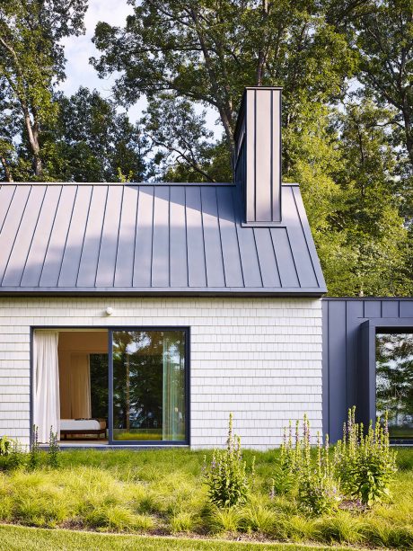 A modern, minimalist home with a striking black metal roof, crisp white siding, and large windows showcasing the lush, natural surroundings.