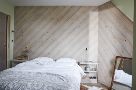 Rustic bedroom with diagonal wood paneling, white bedding, and nightstand.