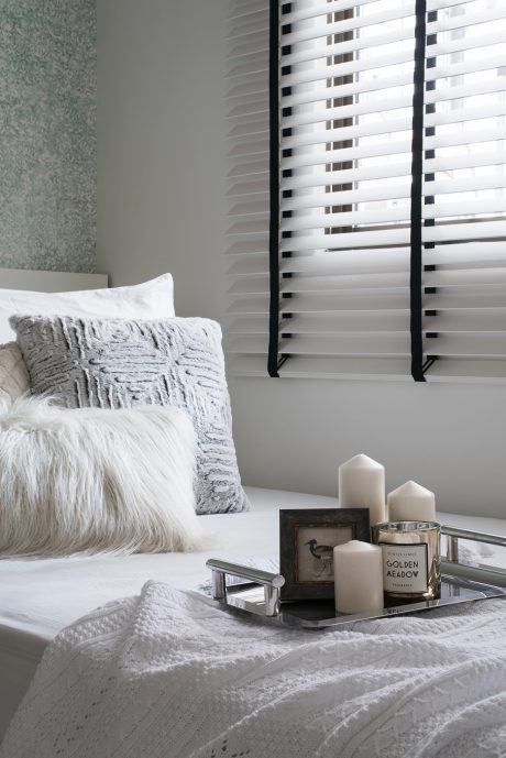 Cozy gray-toned bedroom with plush pillows, candles, and blinds on window.