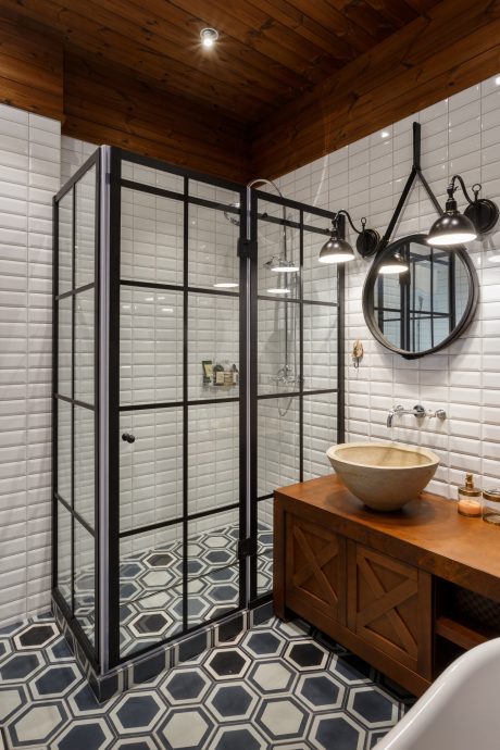 Rustic bathroom with black-framed glass shower enclosure, hexagonal floor tiles, and vanity.