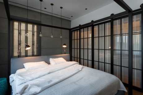 Monochrome bedroom with sleek glass-paned walls, pendant lighting, and a cozy bed.