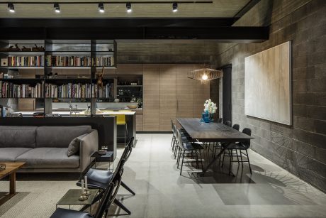 Modern and minimalist open-concept living space with bookshelves, dining table, and industrial-style lighting.