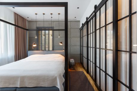 Minimalist bedroom with concrete walls, black framed windows, and pendant lighting.