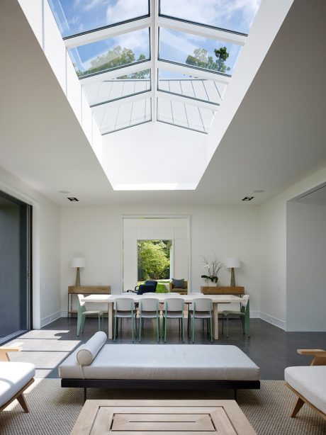 Bright, modern interior with glass skylight, sleek furniture, and tranquil garden view.