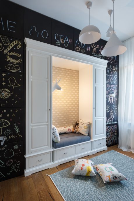 A stylish children's room with a built-in nook, chalkboard wall, and playful lighting.