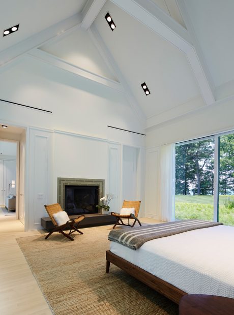 Large vaulted ceiling with exposed beams and recessed lighting, expansive windows overlooking lush greenery.