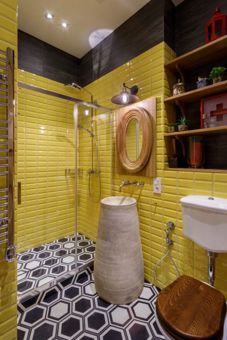 Vibrant yellow tiles, geometric floor, wood accents, and a concrete sink basin create a visually striking bathroom design.