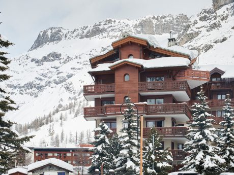 Picturesque alpine chalet with ornate wooden balconies, set against a snowy mountain backdrop.