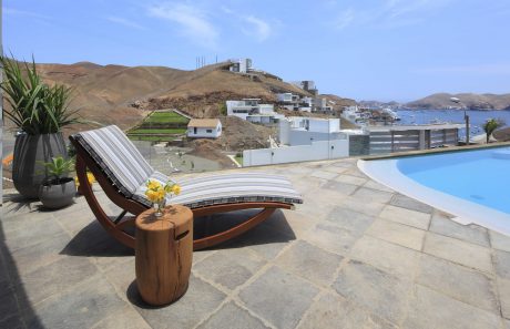 A poolside lounger with wooden accents against a backdrop of Mediterranean architecture.