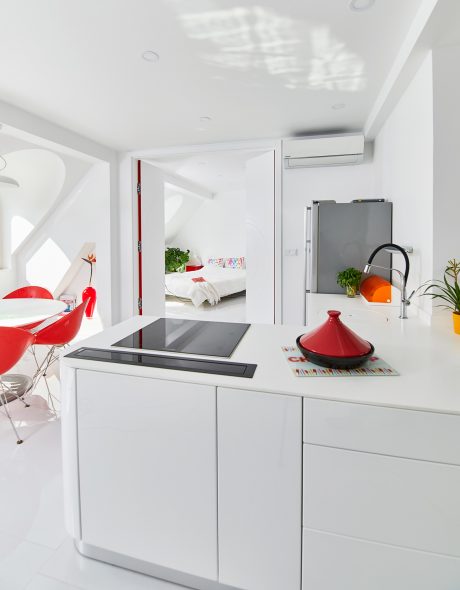 Vibrant red accents complement the minimalist white kitchen design with modern appliances.