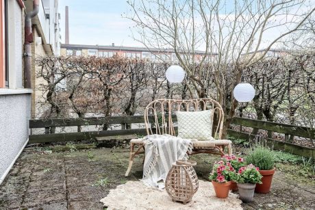 Cozy patio with rustic wicker chair, potted plants, and paper lanterns amid bare trees.
