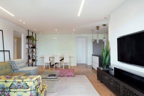 Bright open-concept living room with modern furniture, shelving, and lighting fixtures.