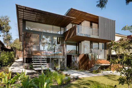 Modern two-story home with wooden slat exterior, expansive glass walls, and lush landscaping.