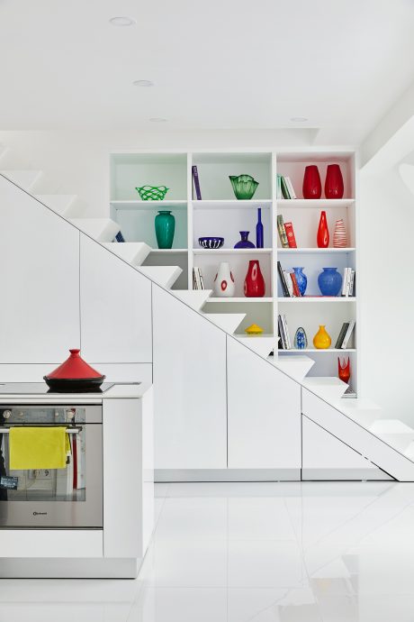 A modern, minimalist kitchen with a unique shelving unit displaying colorful glassware.