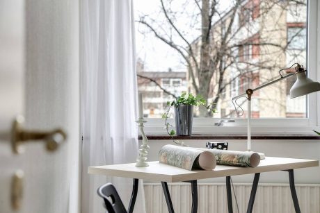 A cozy home workspace with a minimalist desk, houseplant, and view of trees through the window.