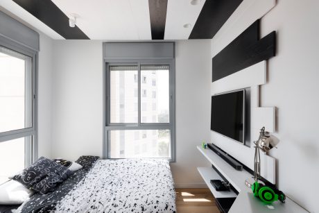 Minimalist bedroom with modern black and white decor, large window, and built-in TV stand.