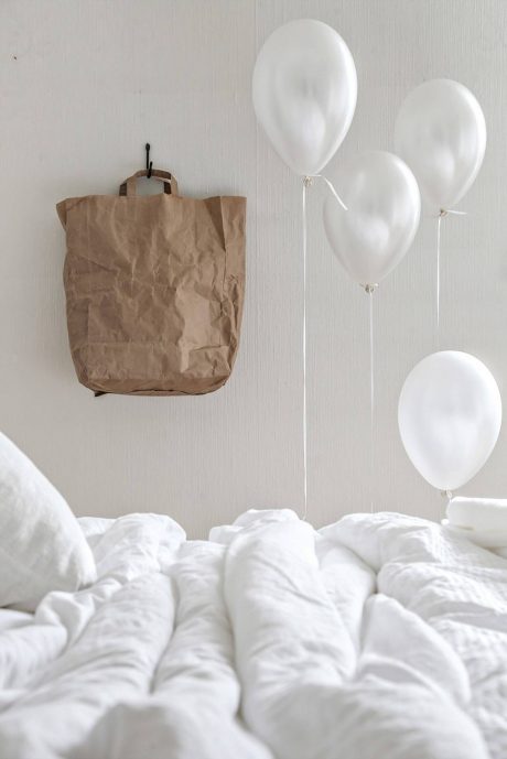 A crumpled brown paper bag and white balloons against a plain, white interior.