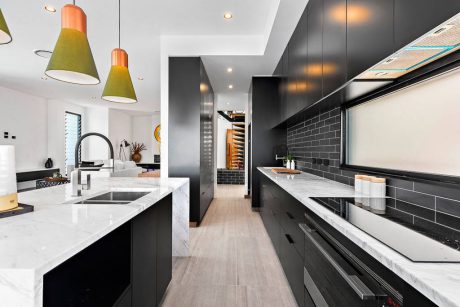 Modern kitchen with sleek black cabinets, white countertops, and vibrant pendant lights.