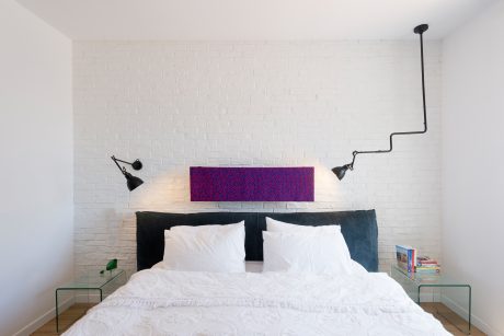 Minimalist bedroom with white brick wall, black headboard, and modern light fixtures.