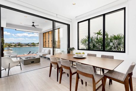 Spacious open-concept living area with large windows overlooking the water and lush greenery.