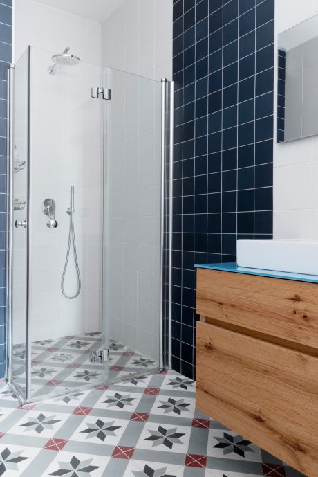Modern bathroom with sleek glass shower enclosure, patterned tile floor, and wooden vanity.